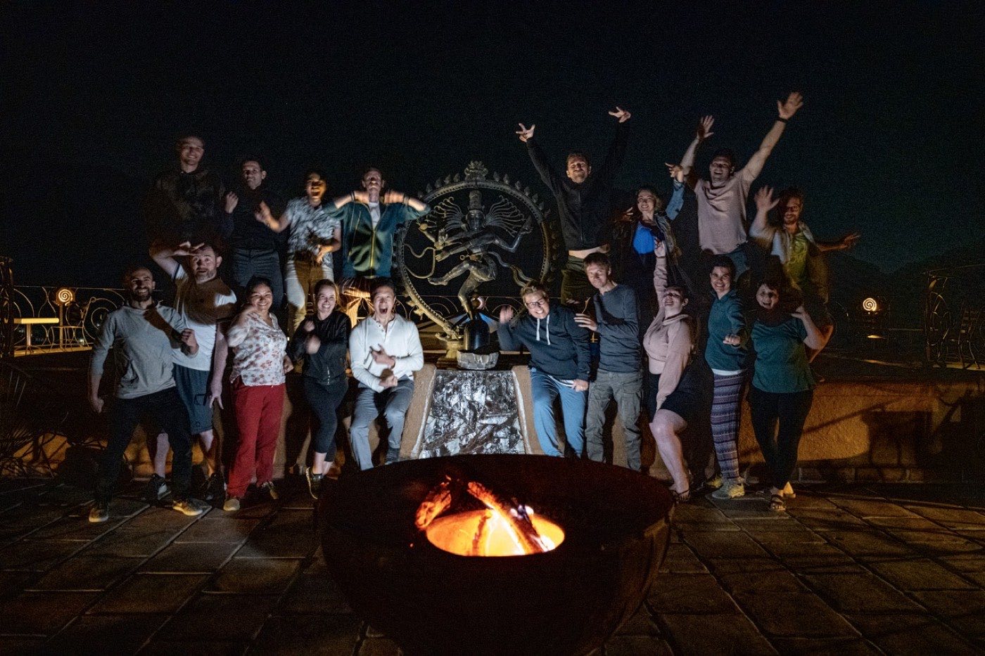Celebrating group at night around the fire bowl, a large sculpture behind