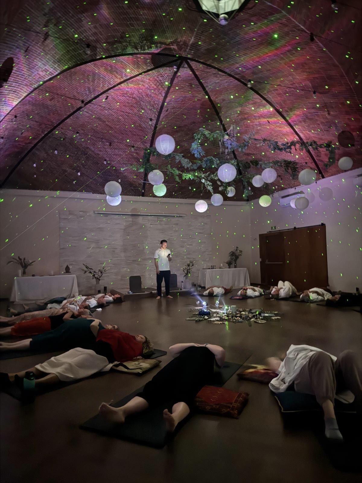 Breathwork under the domed ceiling, the group lying in a circle beneath paper lanterns and a starry light