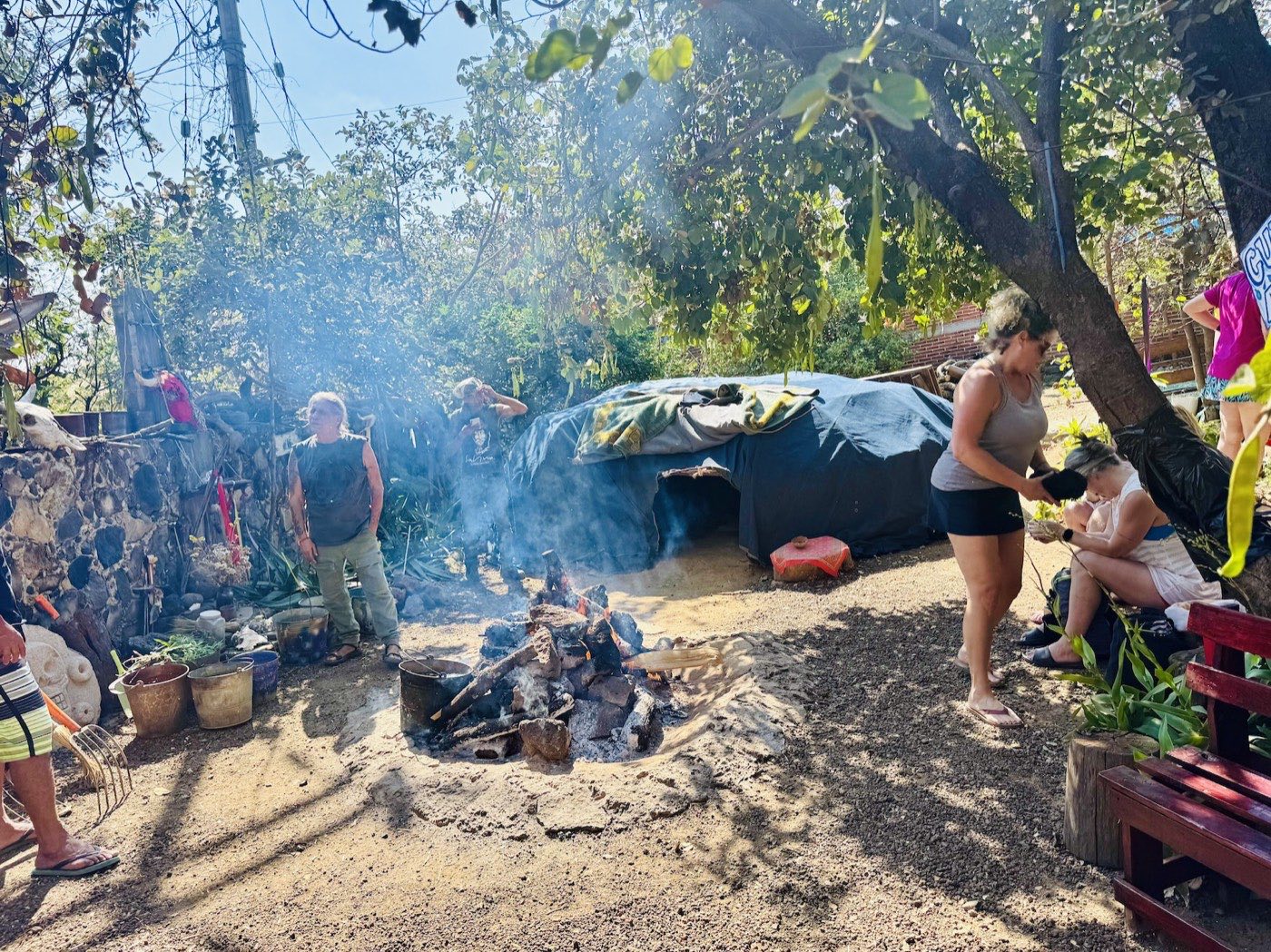 Wider daytime fire scene with smoke and temazcal