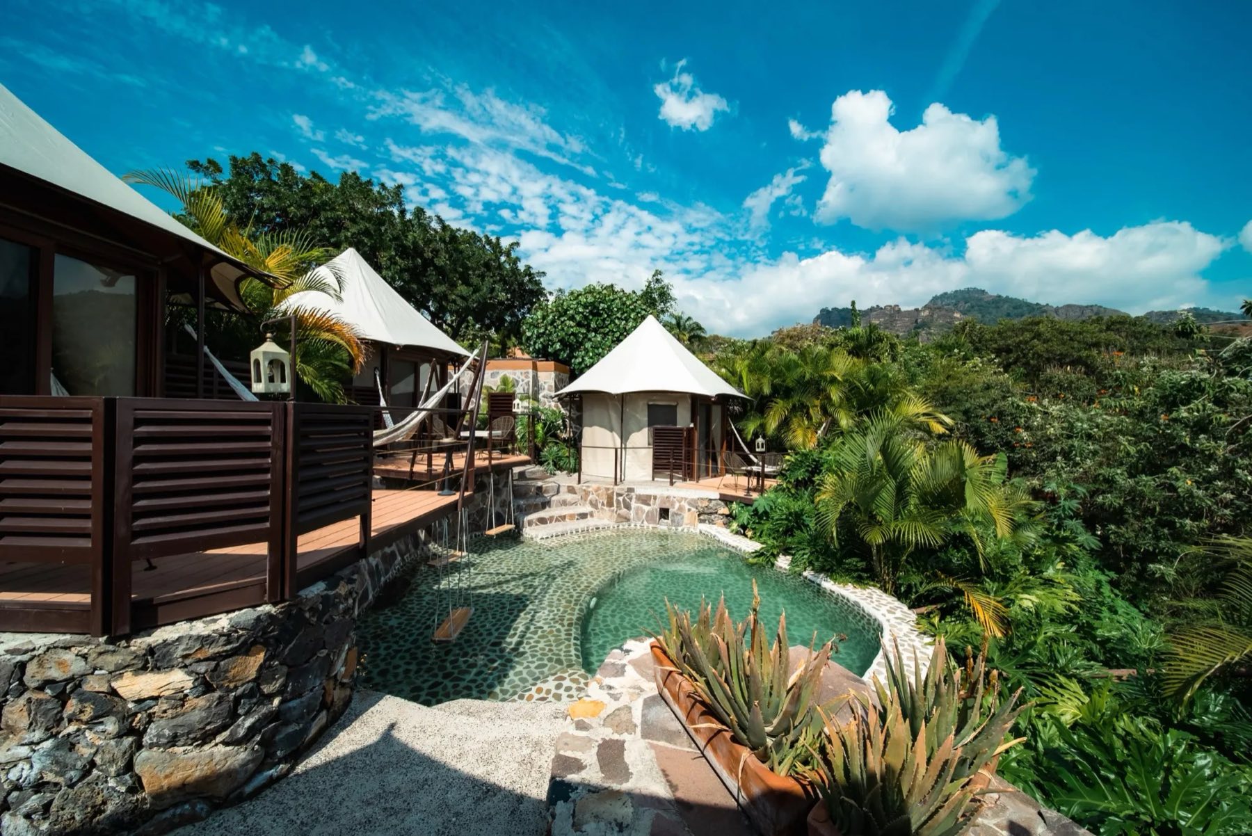 Canvas tents and a stone pool in the gardens, the mountains behind